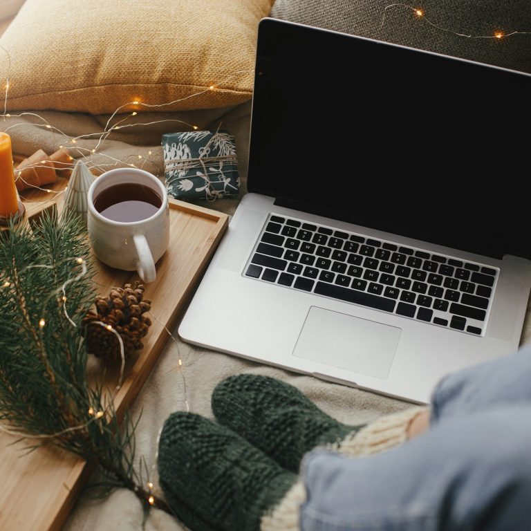Jemand sitzt mit Wollsocken, Tee und Weihnachtsdekoration neben dem Laptop.